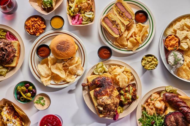 Plates across a table: brisket sandwich, the L&L burger, tacos, smoked chicken, cauliflower burnt ends, kimchi and sausage