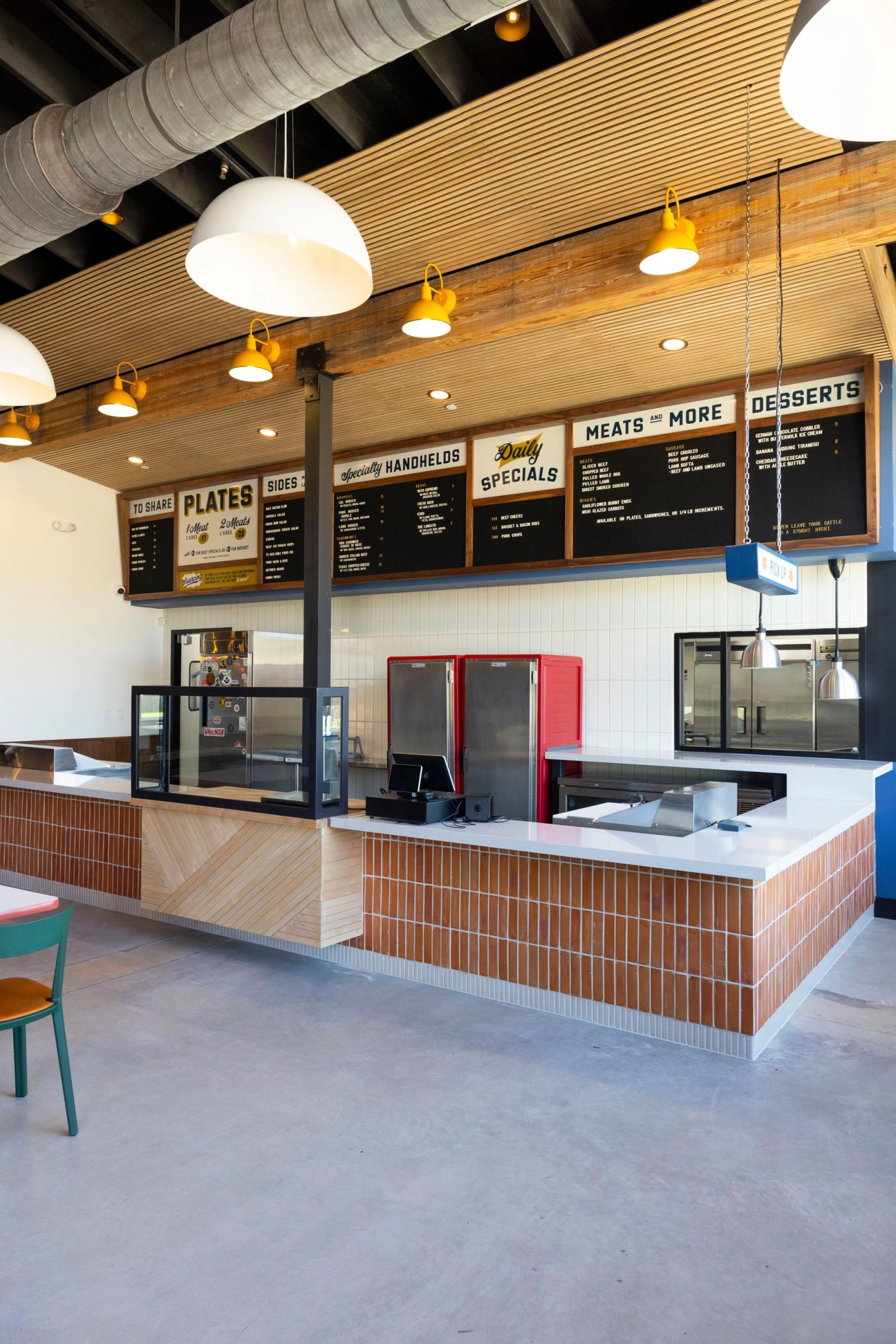 The LeRoy and Lewis order counter under the menu boards — Plates, Sides, Specialty Handhelds, Daily Specials, Meats and More, Desserts — with red fridges behind