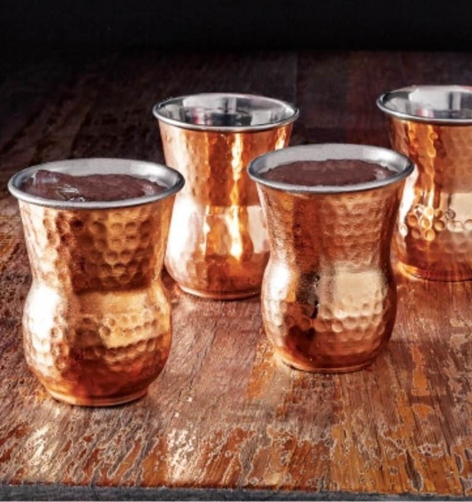 Four hammered copper tumblers on a wooden table