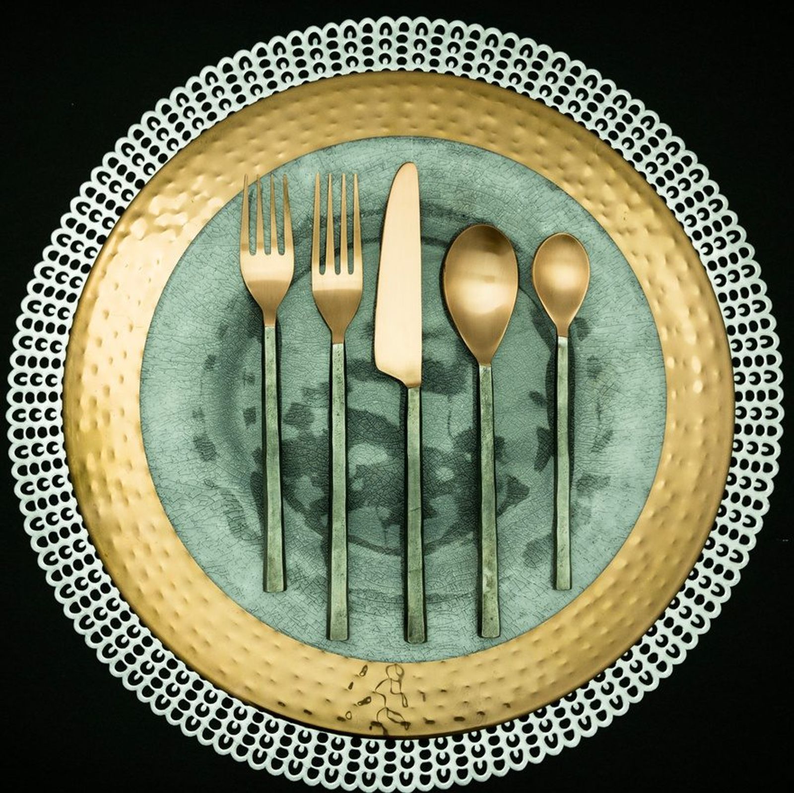 Brushed-brass flatware on a sage ceramic plate with a beaded charger