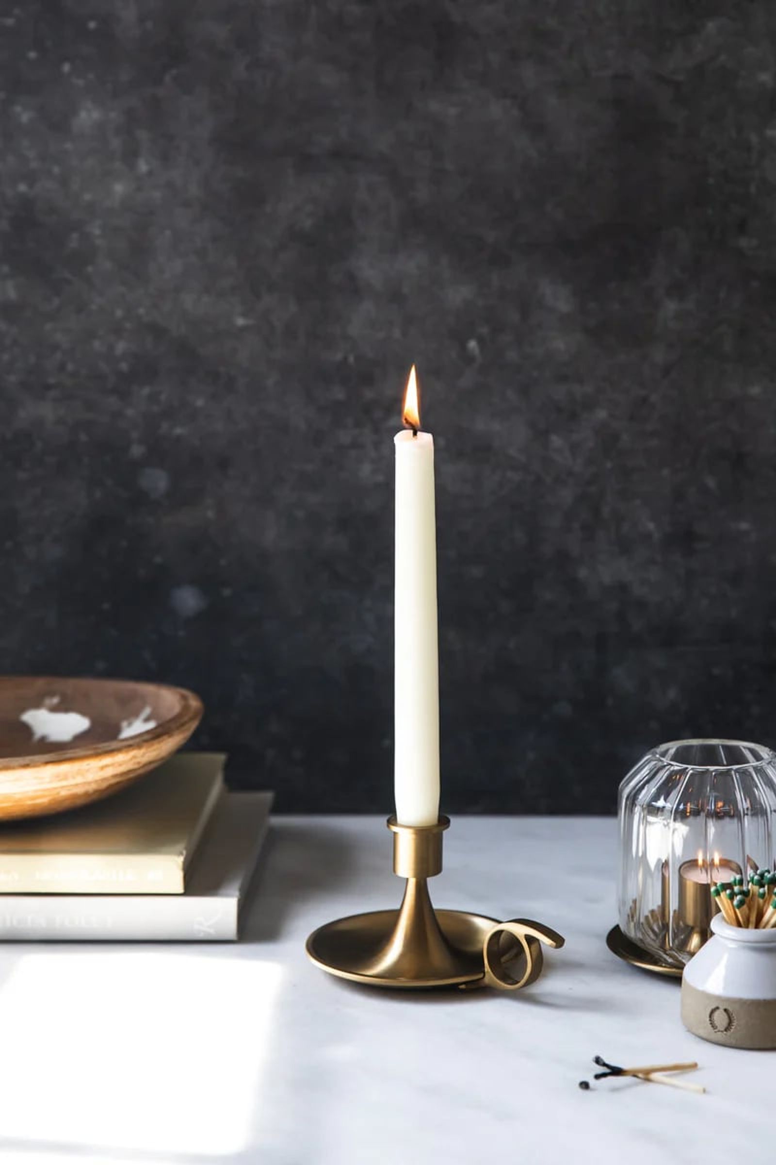 Brass chamberstick with a taper candle, styled against a dark ground
