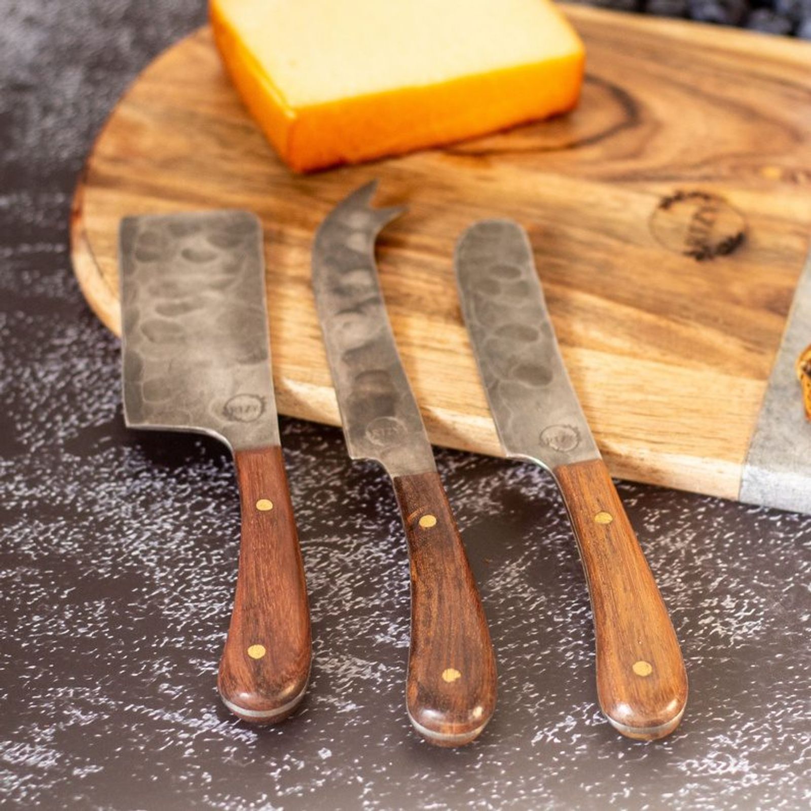 Hammered cheese knives on a wooden board with cheese