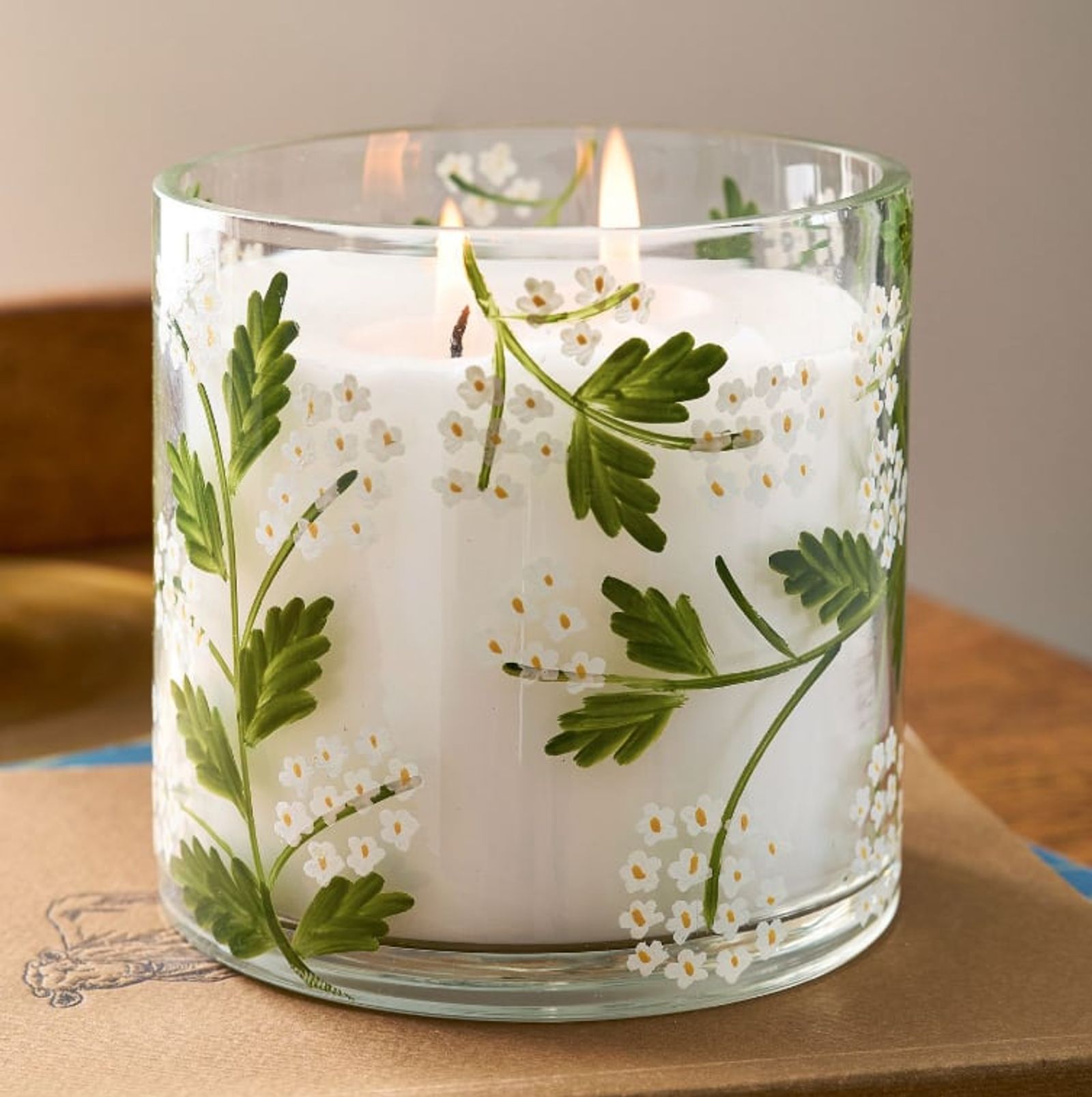 Lit candle in a glass vessel with pressed white botanicals