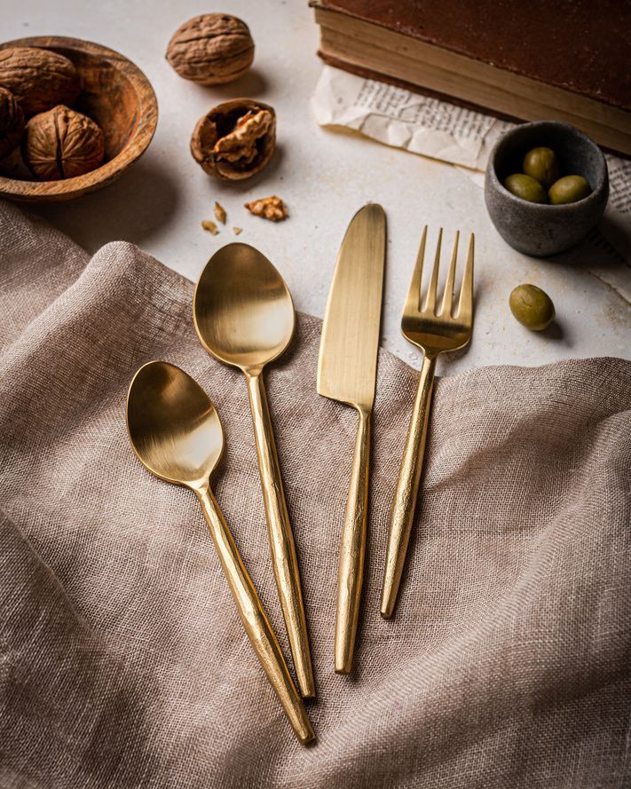Brushed-gold flatware styled on linen with walnuts