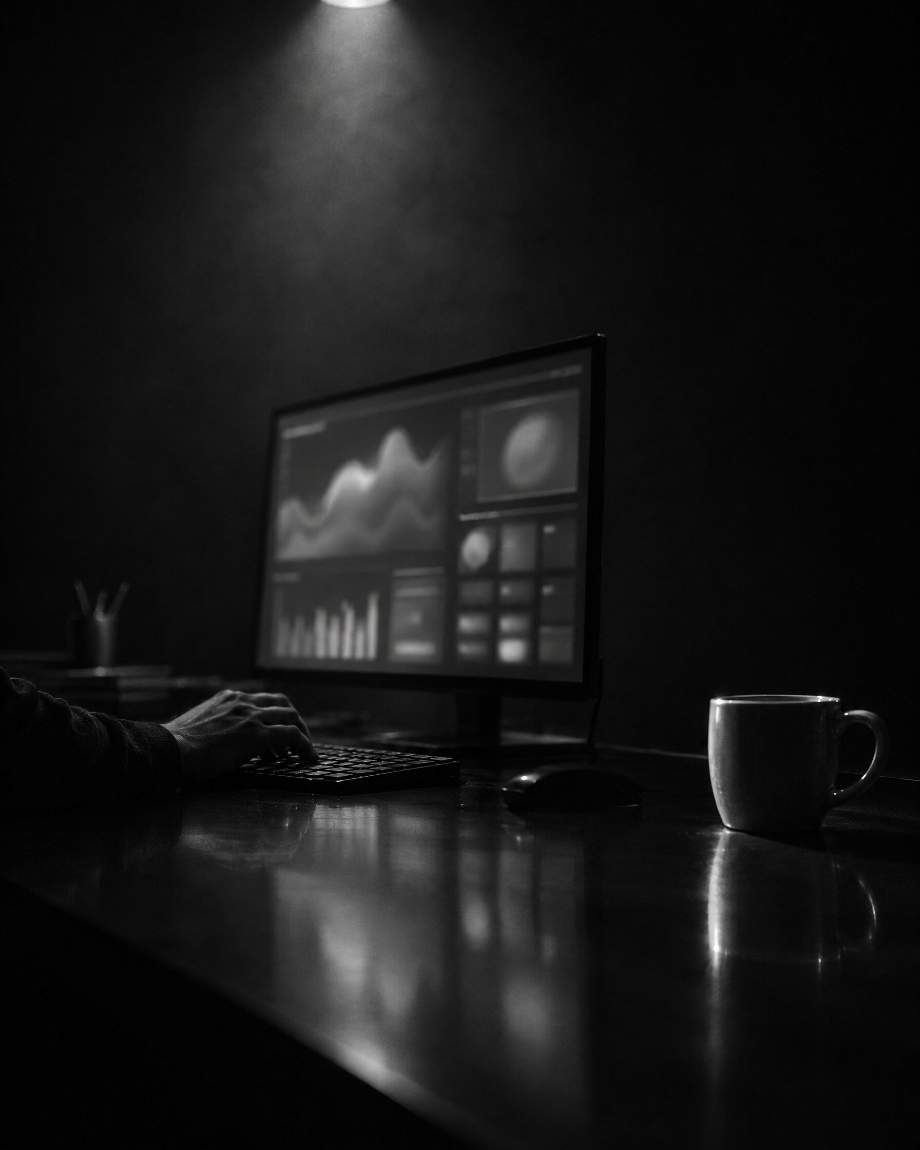 Dłoń na klawiaturze przy monitorze z rozmytymi wykresami monitoringu w ciemnym pokoju
