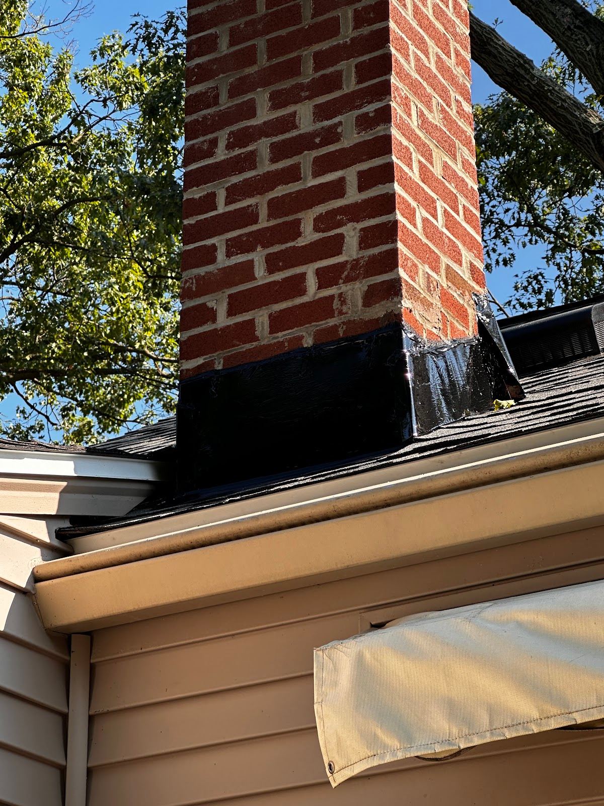 A new shingle roof meeting its gutter along the eave, beside a brick chimney