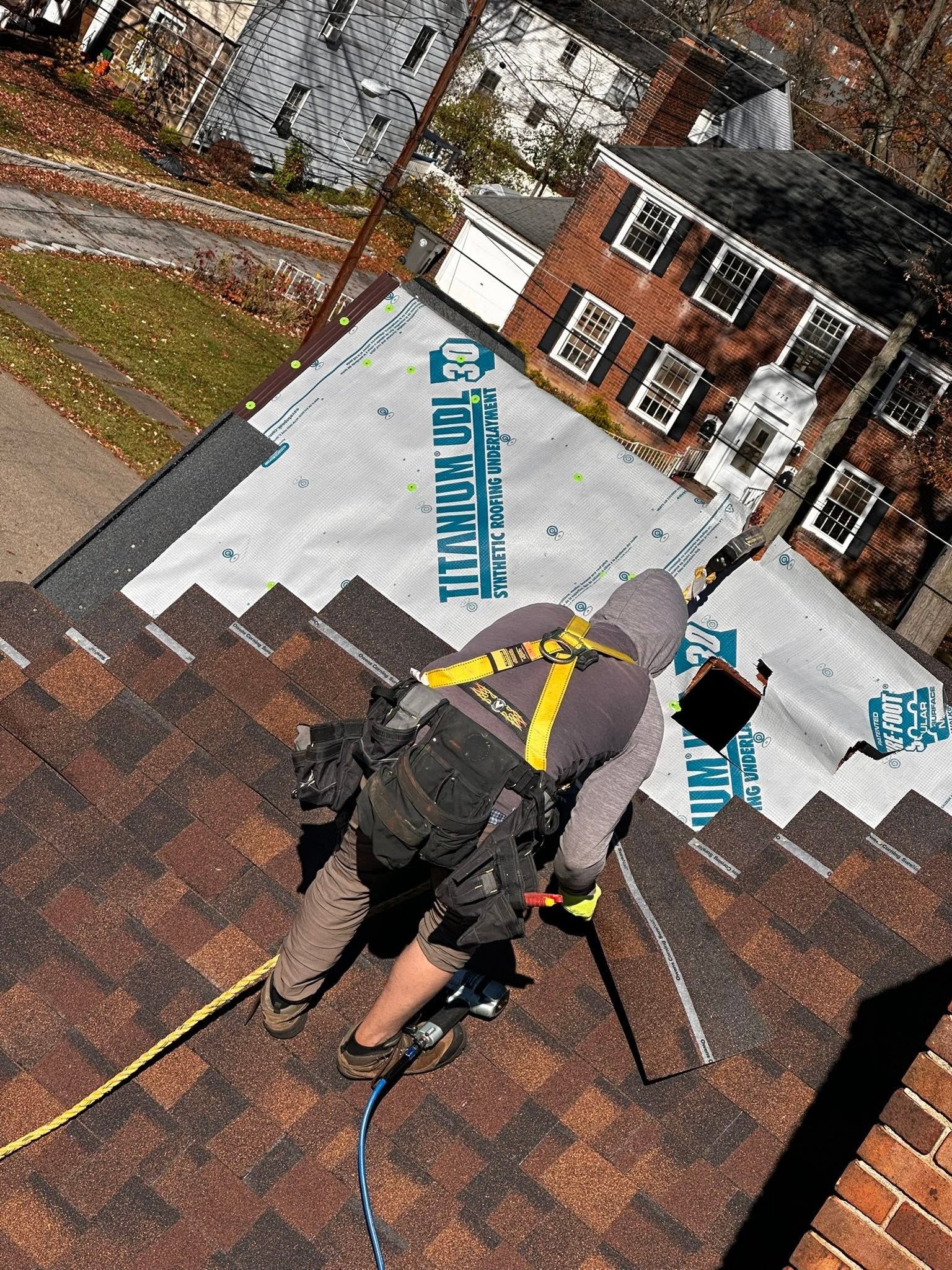 A roofer in a harness laying brown shingles over synthetic underlayment