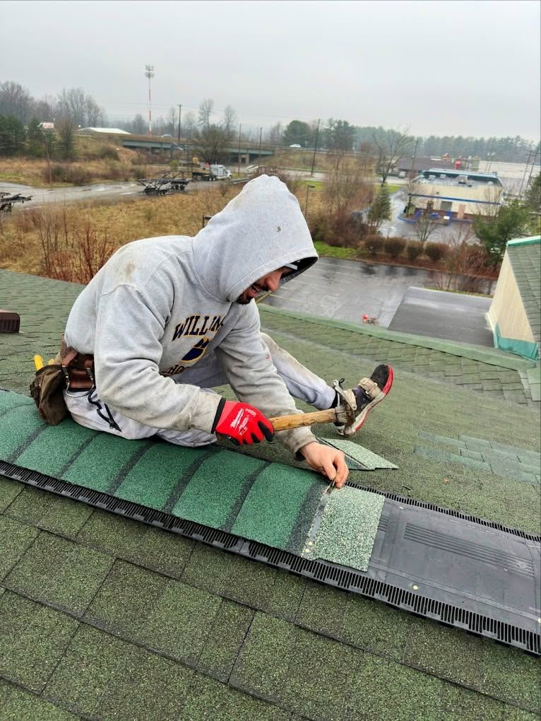 A roofer nailing new green shingles by hand, up near the ridge