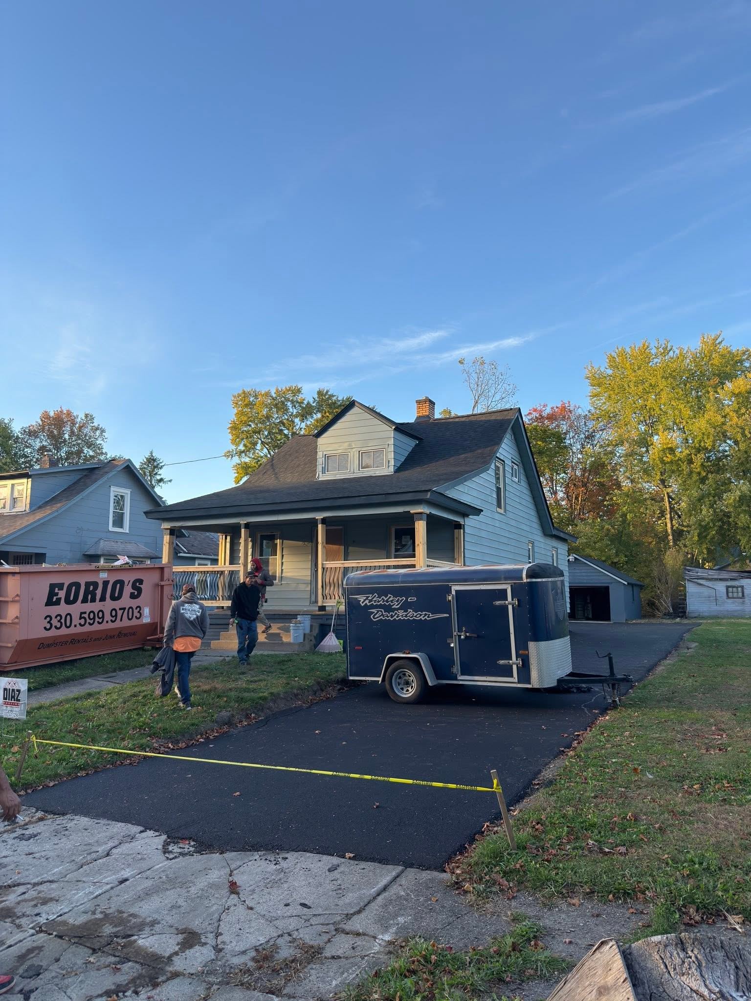 A house mid-job, with a dumpster and work trailer in the driveway and the crew in the yard