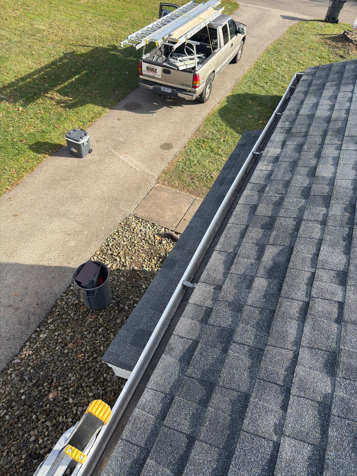 A gutter along the eave, seen from the roof, with the truck and ladders in the driveway below