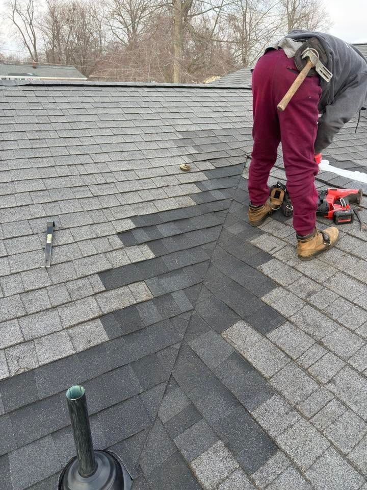 A roofer nailing new shingles into an older gray roof