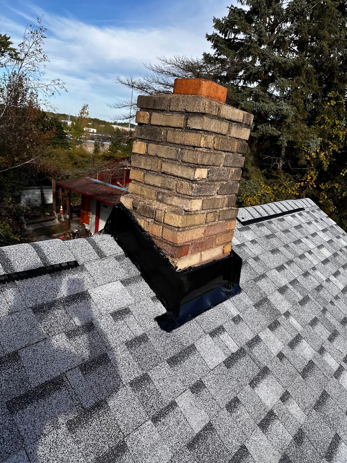 A yellow-brick chimney with new flashing, set into a new gray shingle roof