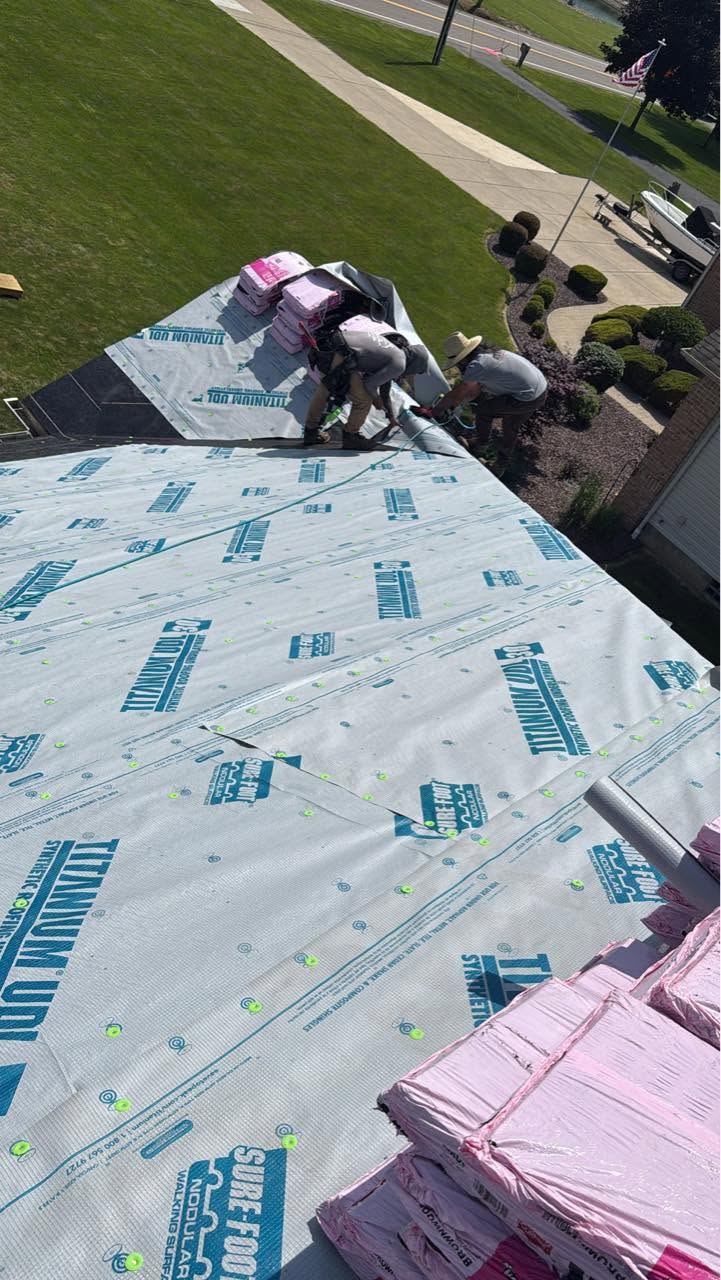A roof covered in synthetic underlayment, with shingle bundles and the crew at the far end