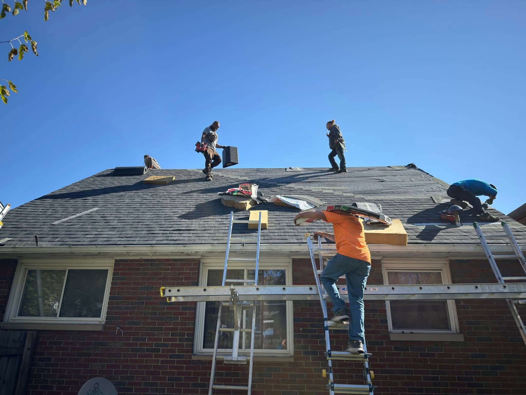 A crew on the roof of a brick building, with ladders up the front wall