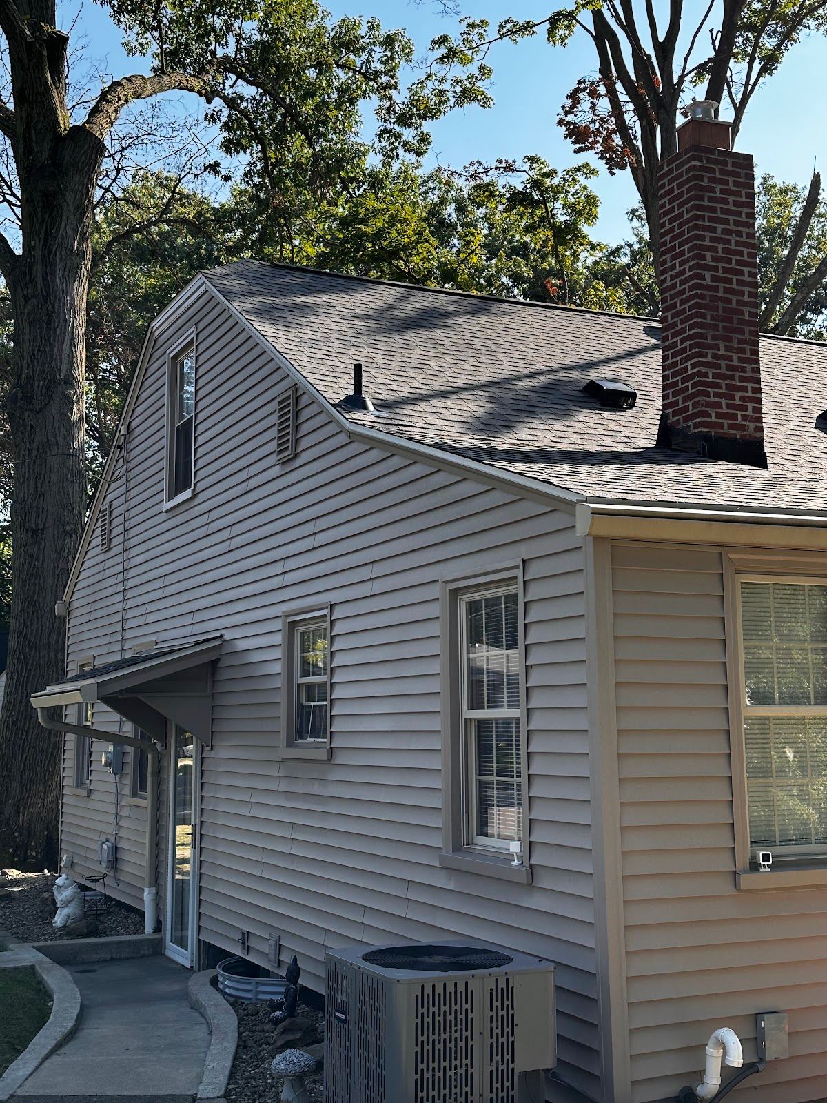 A new shingle roof with its vents and chimney, over a sided house