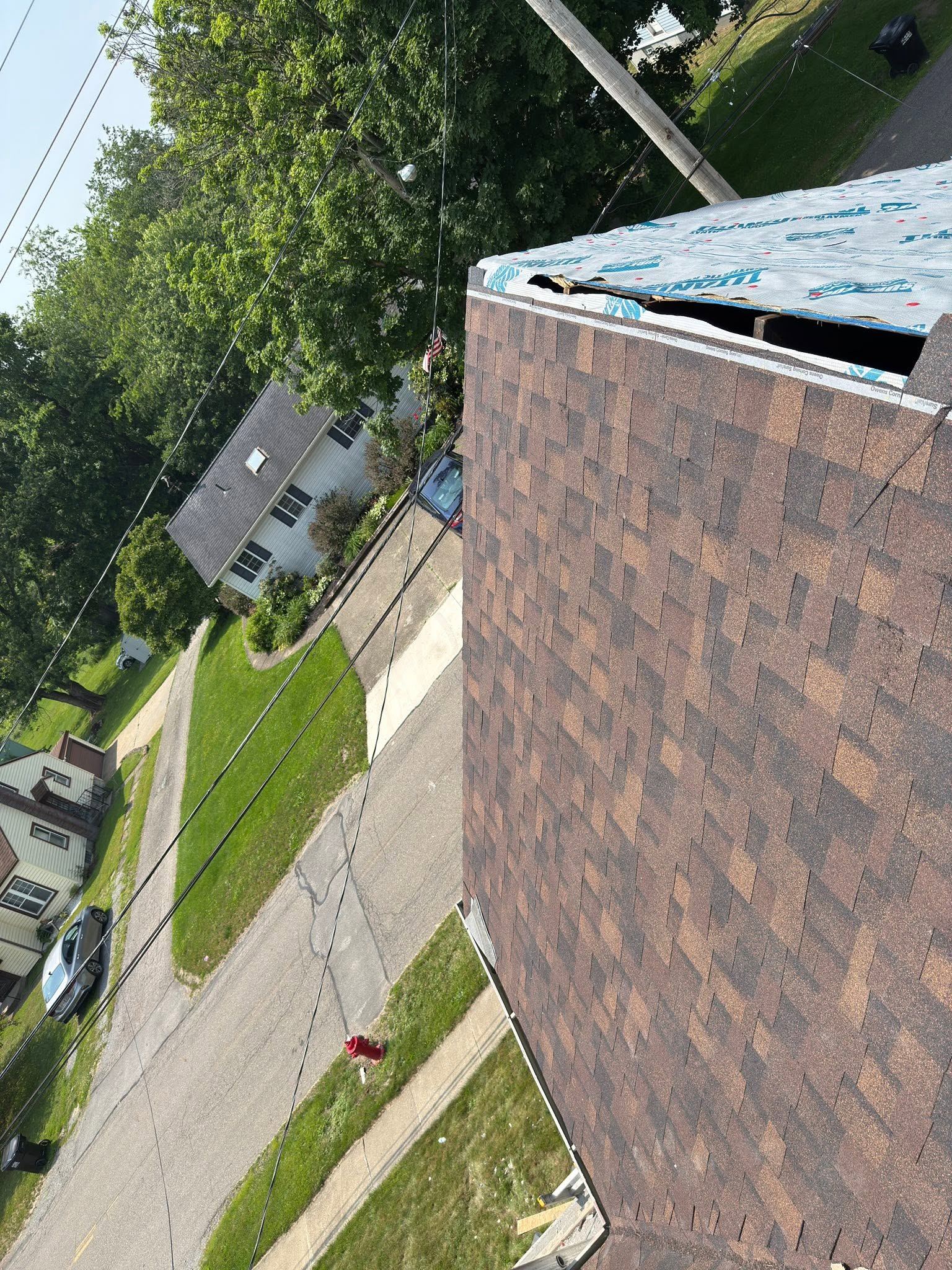 The edge of a new brown shingle roof, high above the street