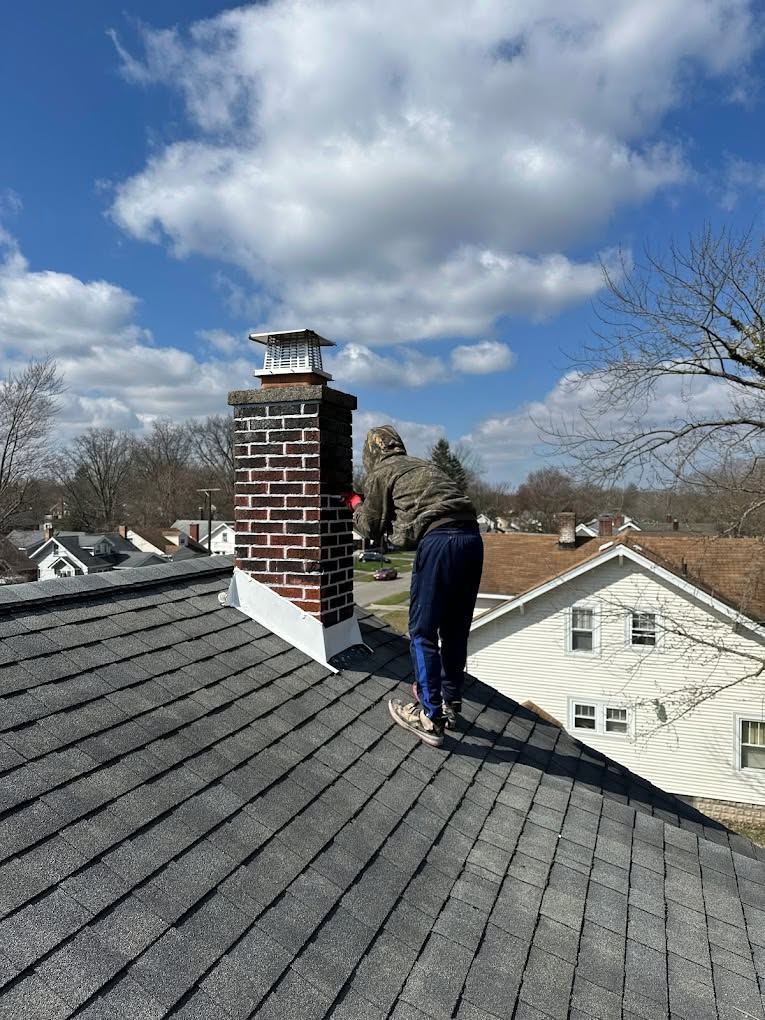 Roofers at work beside a brick chimney on a gray shingle roof