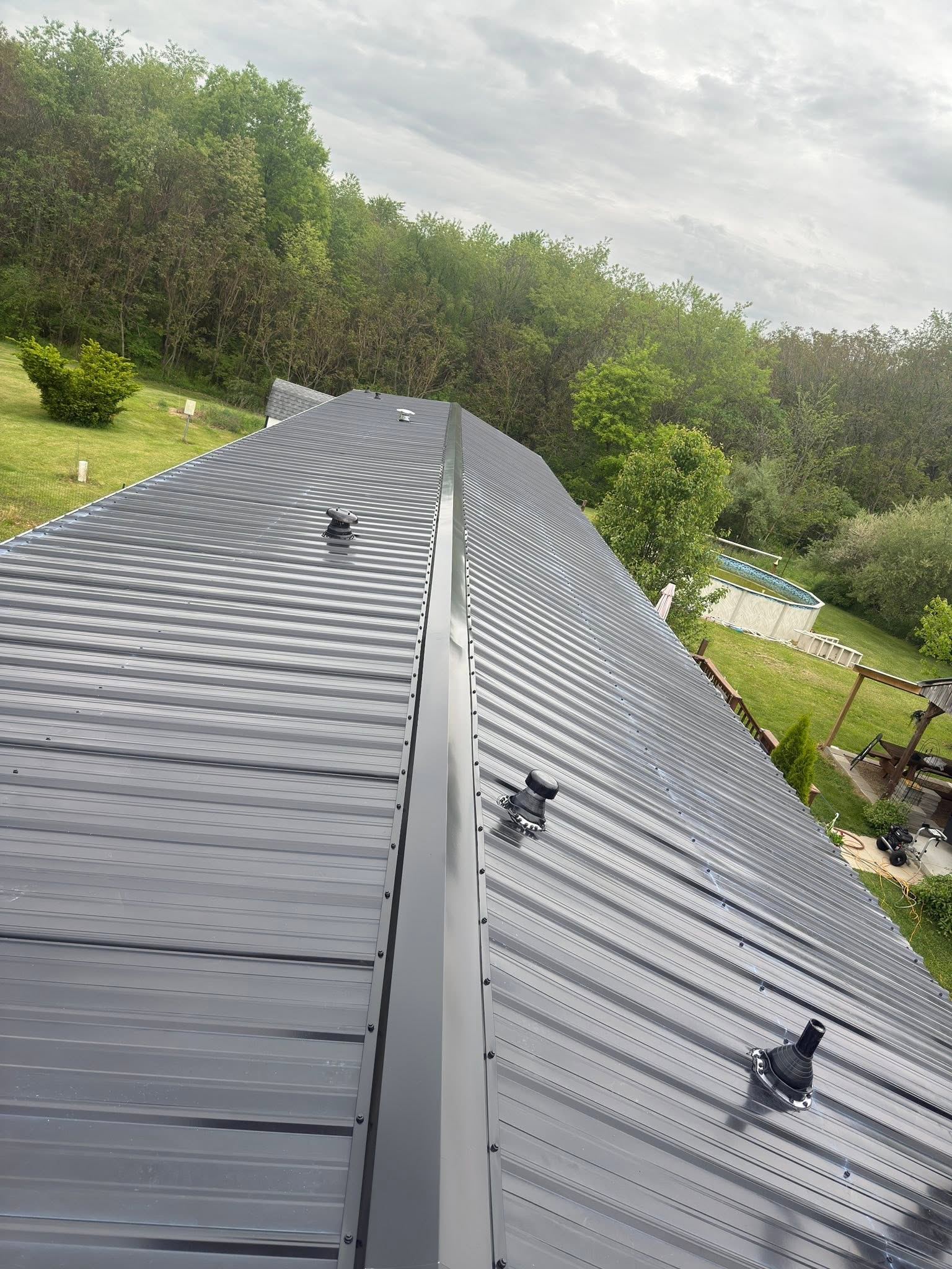 A new dark metal roof with its ridge cap and pipe boots, on a long single-story home