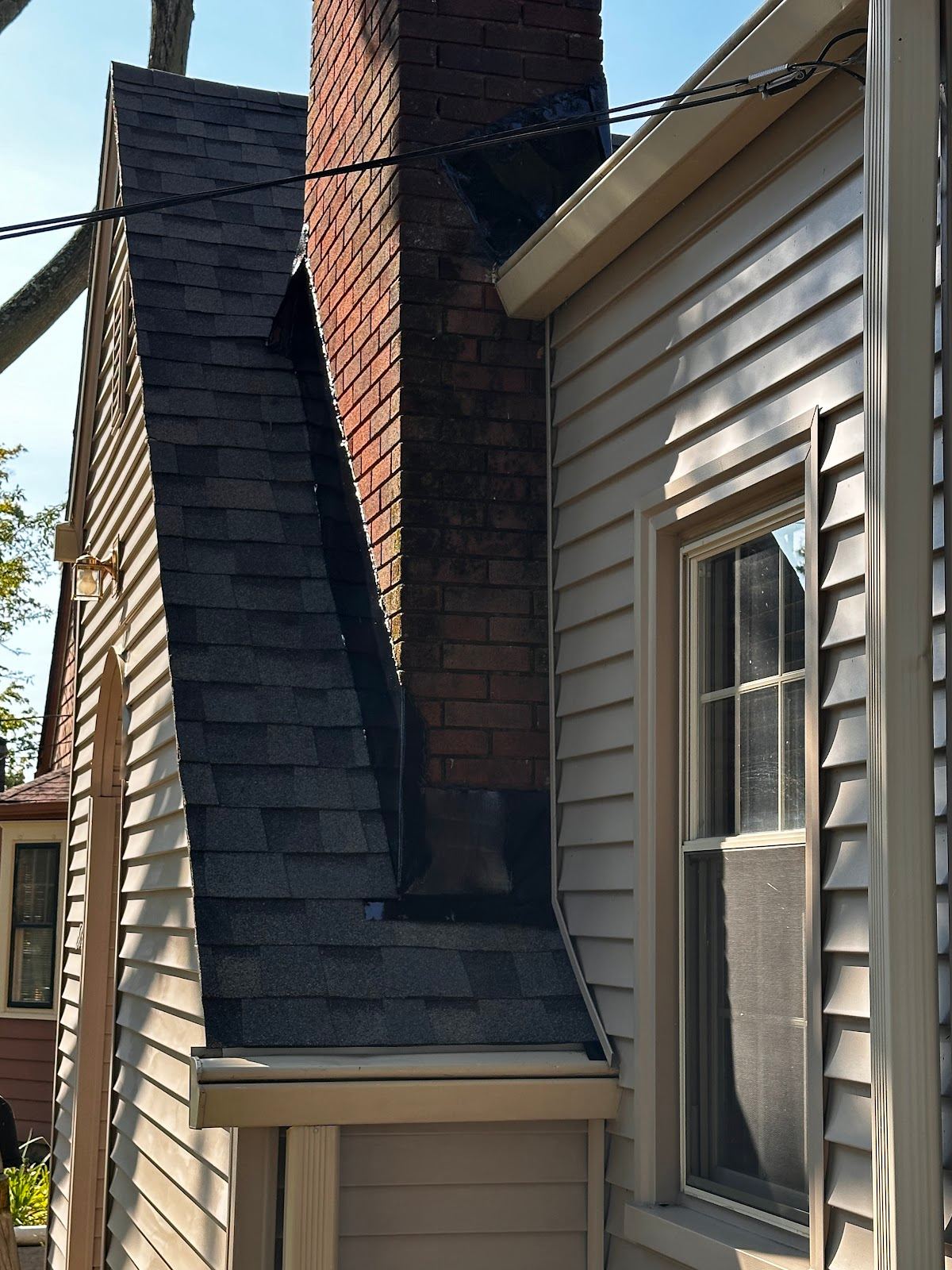 A brick chimney where it meets the shingles and the siding wall