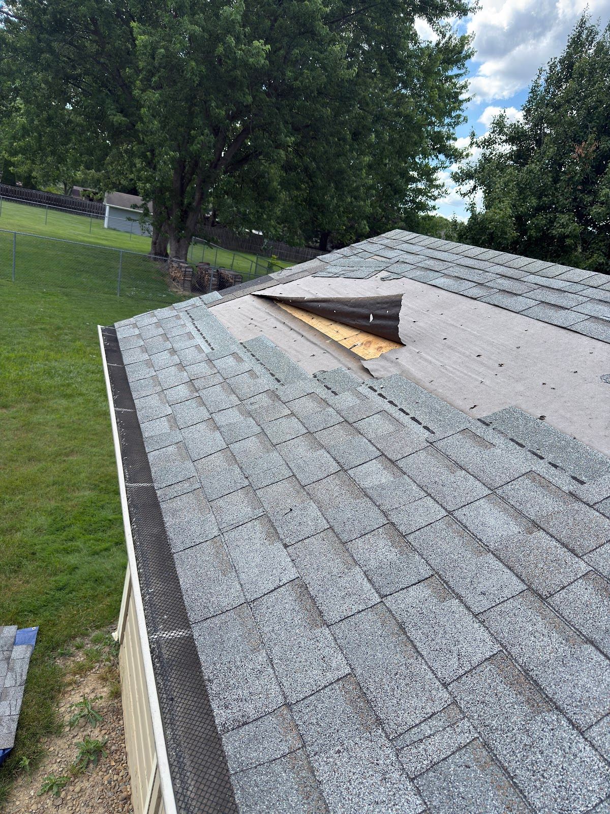 Shingles torn off near the ridge of a gray roof, the underlayment showing beneath