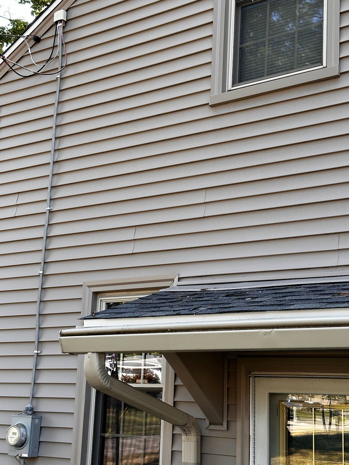 A downspout running down the siding from the gutter above a porch roof