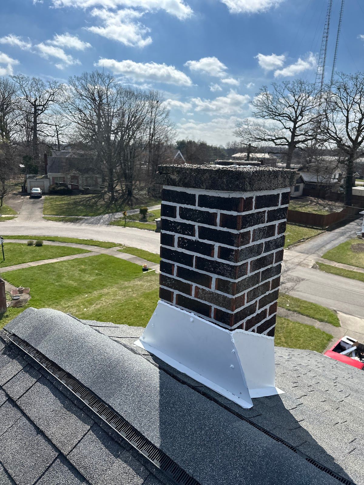 A dark brick chimney with new white flashing at its base, on a new shingle roof