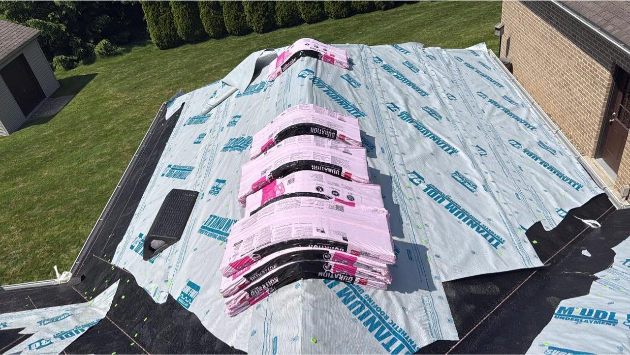 Shingle bundles stacked on the ridge of a roof covered in synthetic underlayment