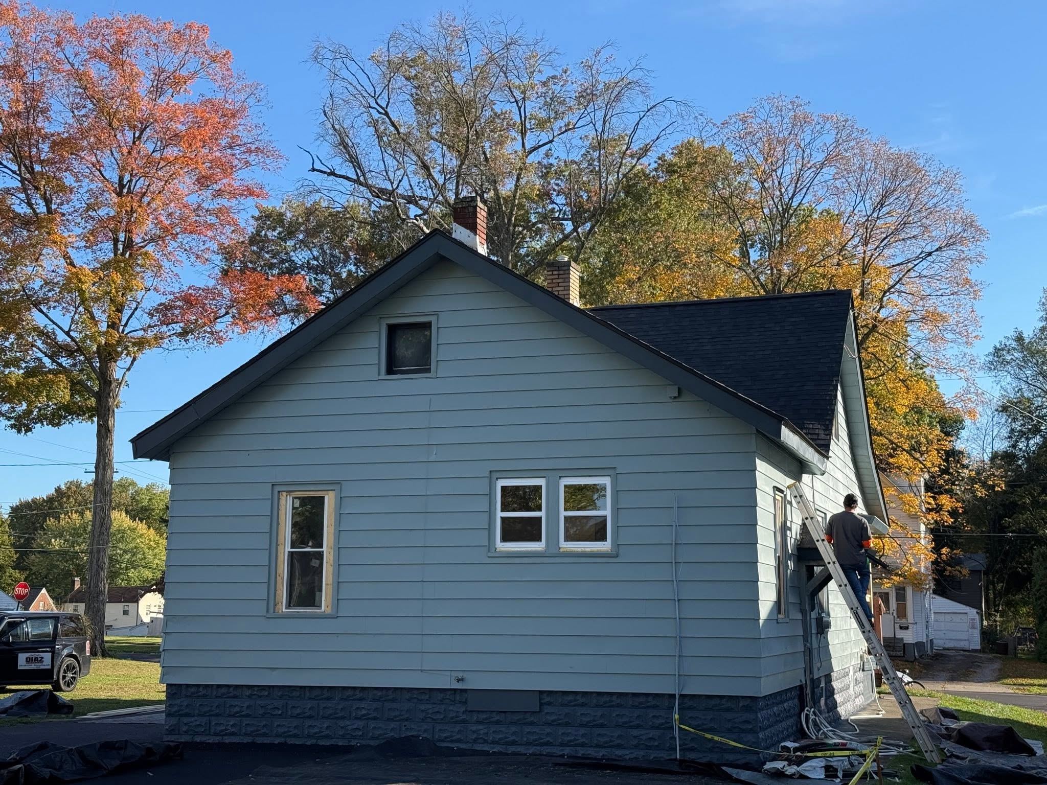 A roofer on a ladder at the eave of a blue house
