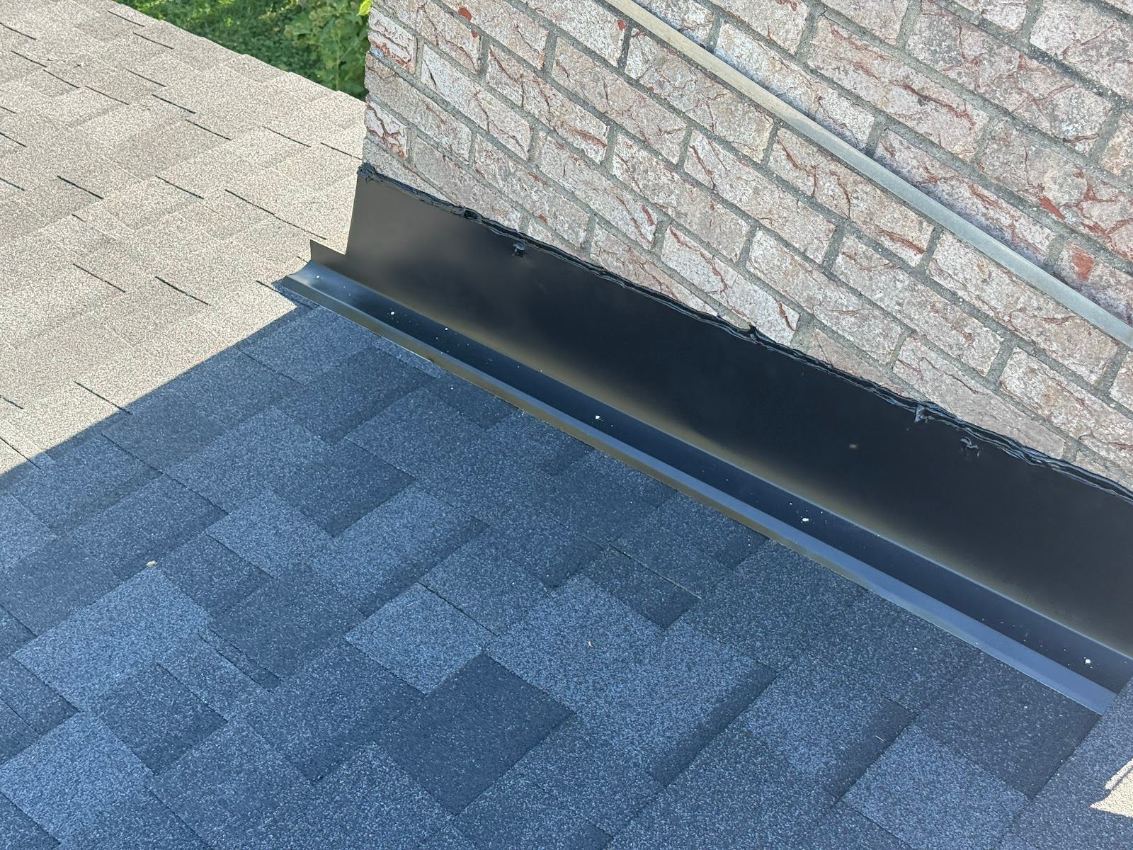 New black metal flashing run along the side of a brick chimney, over new shingles