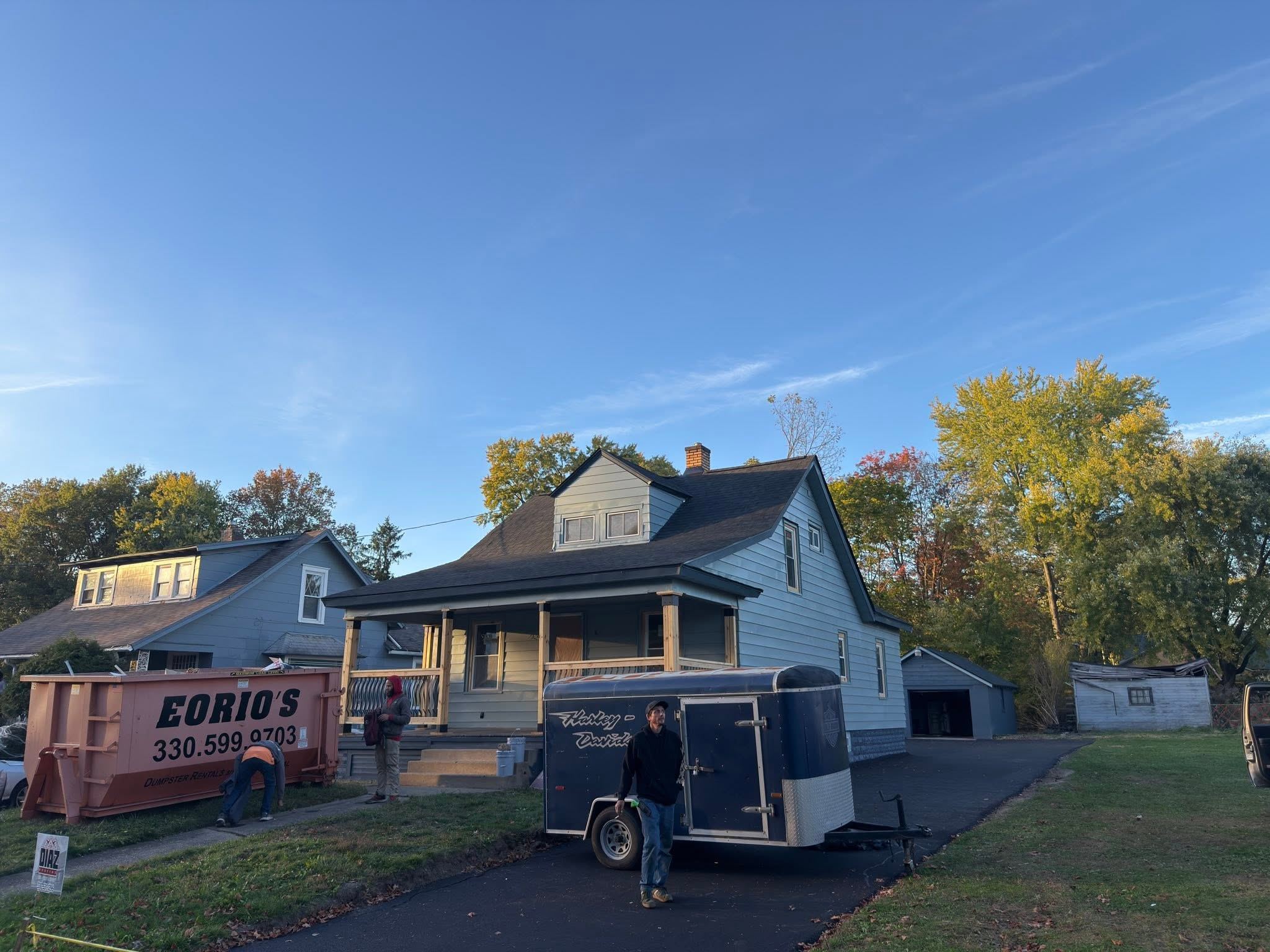 A house from the street during a roof job, dumpster and trailer out front