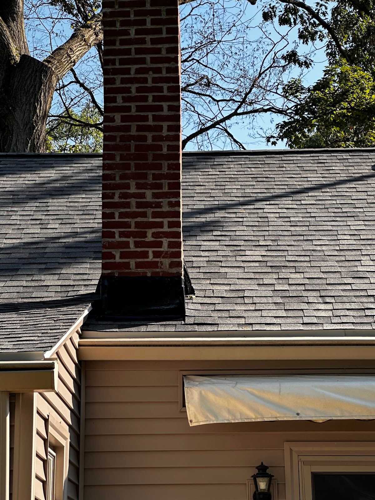 A brick chimney with new black flashing where it meets a new shingle roof