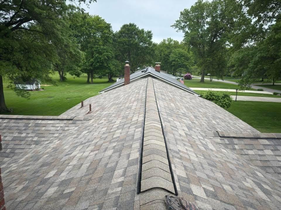 The ridge line of a shingle roof, looking out over the trees