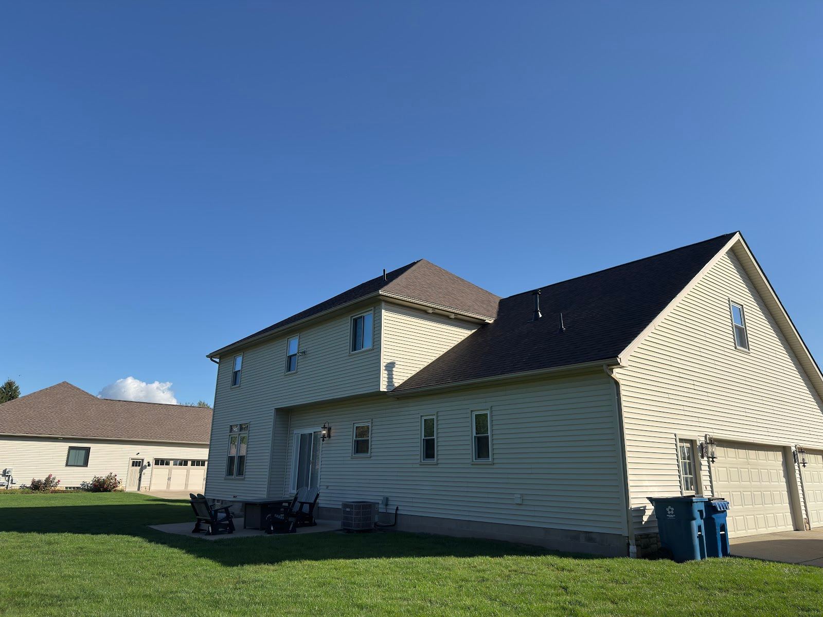 A two-storey sided house with a new dark shingle roof, from the back lawn