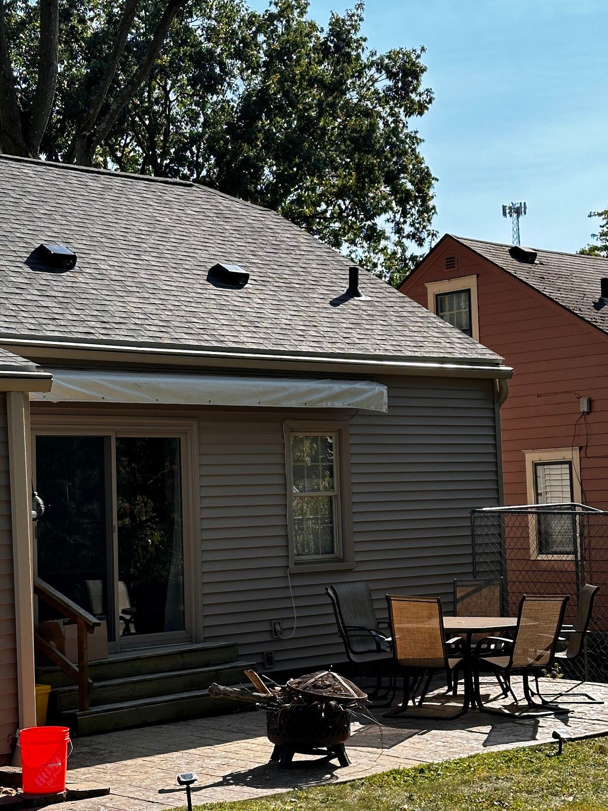 The back of a sided house with a new shingle roof over the patio
