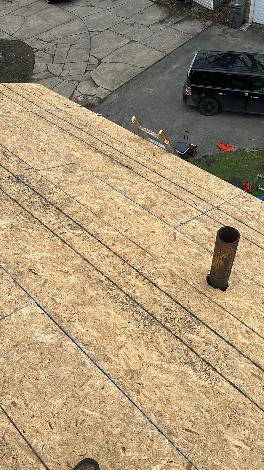 A roof stripped down to the wooden deck, with only the vent pipe left standing