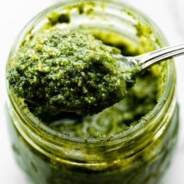 a spoon lifting some pesto out of a glass jar