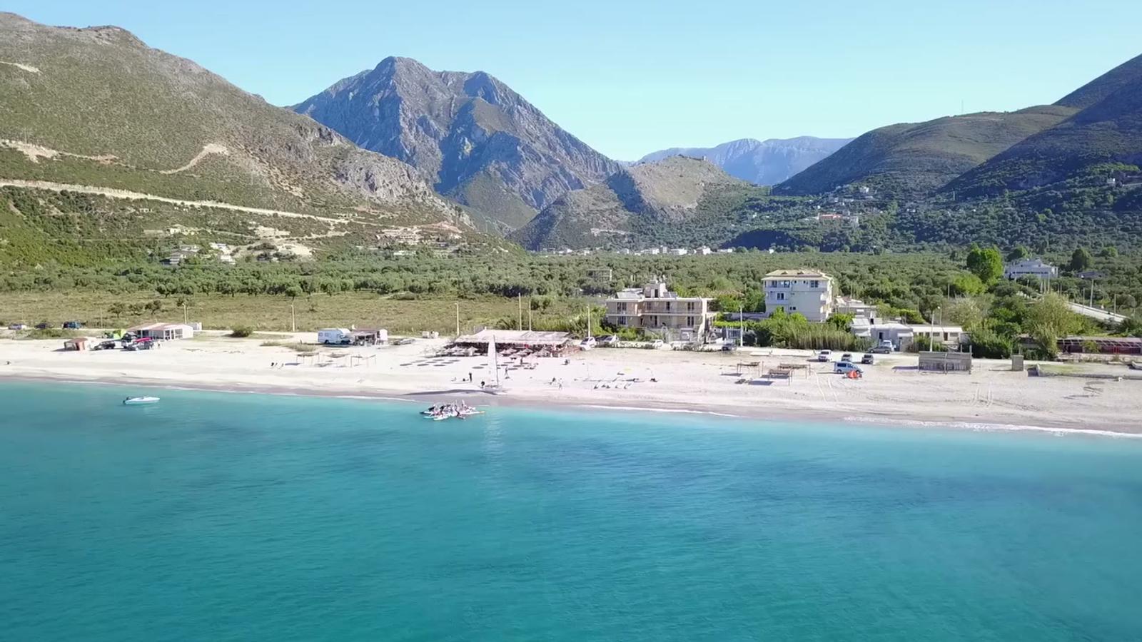 Drone view from the sea over Borsh beach toward Vila Borsh, mountains behind