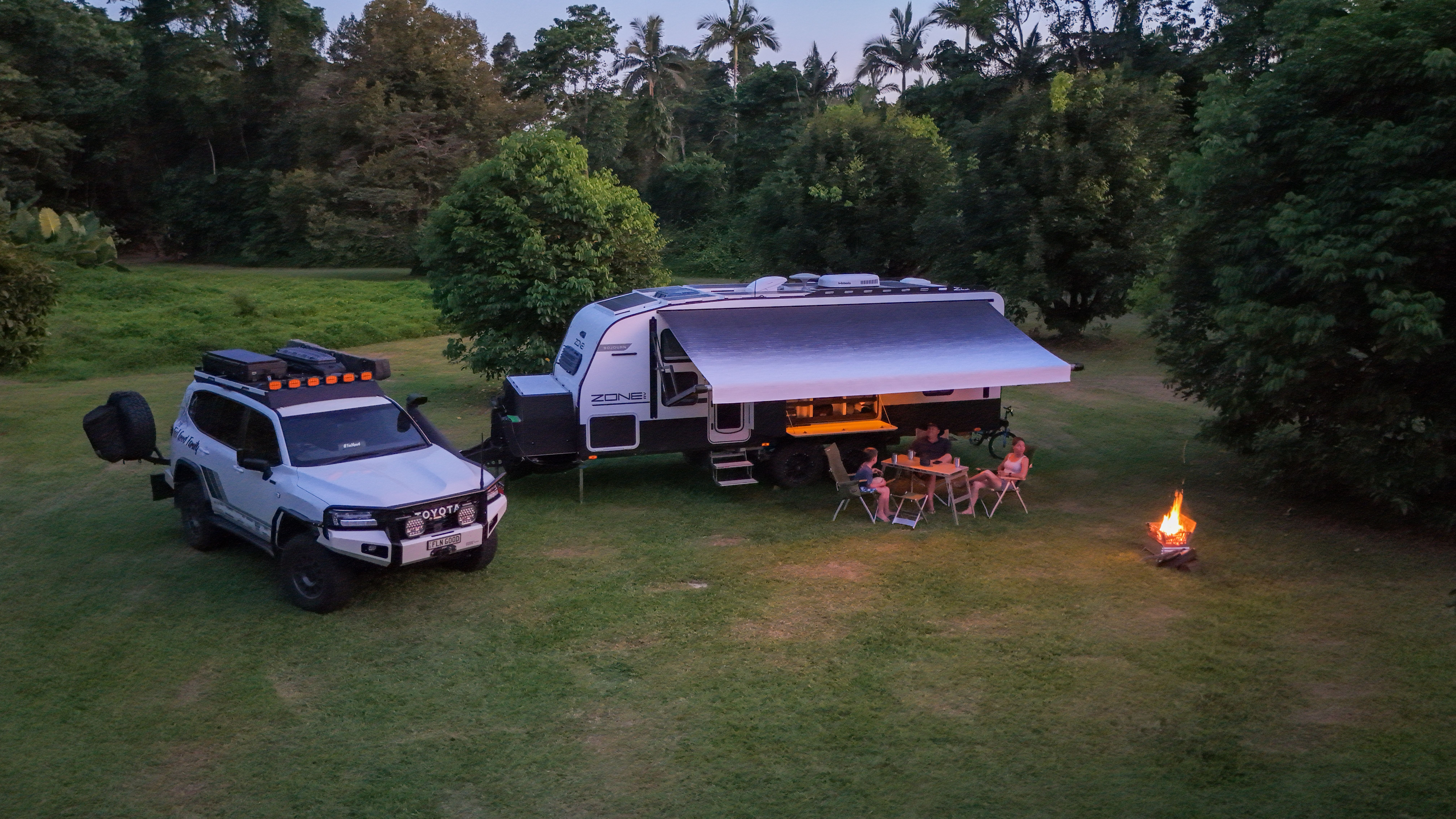 a 4x4 and caravan parked on a campsite with a campfire at sunset