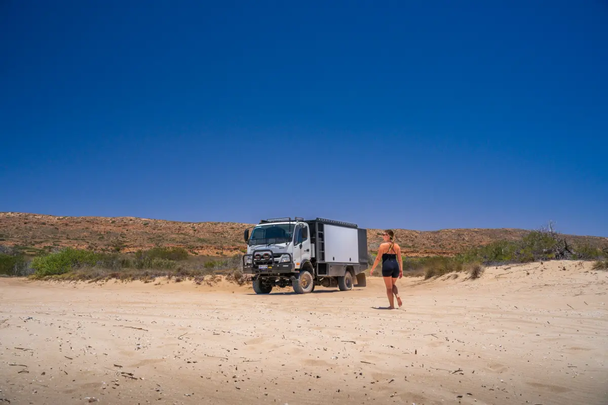 a 4x4 truck on a beach with a woman walking towards it