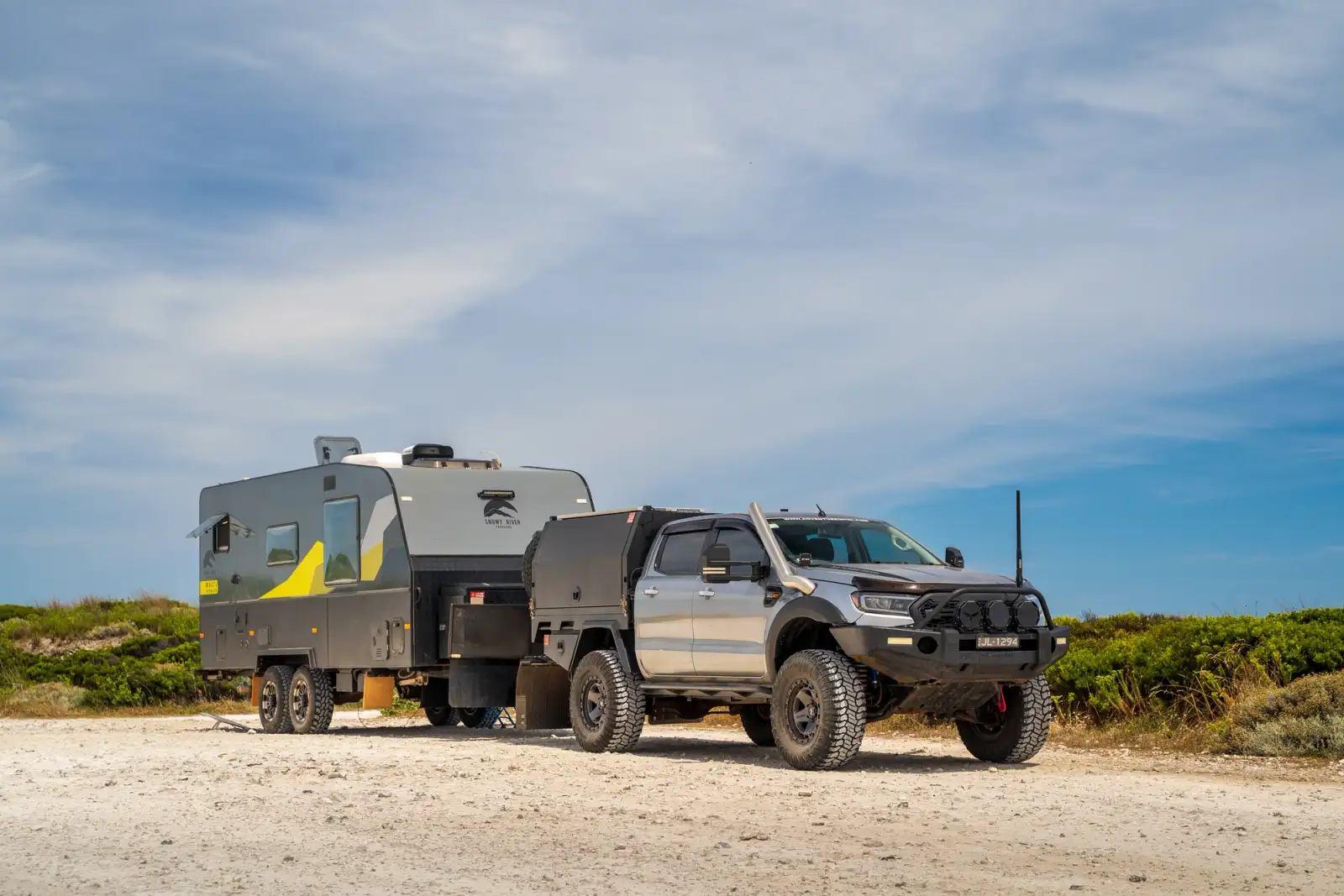 4x4 with a caravan on sand with shrubs behind