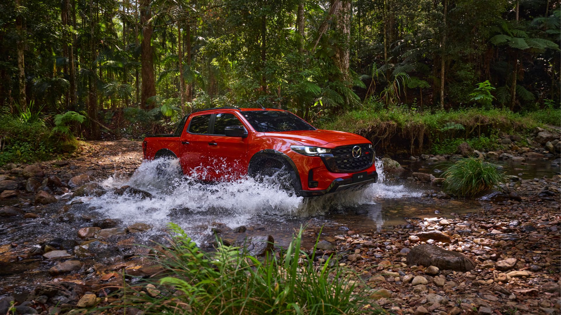 A red 2025 Mazda BT-50 driving through water