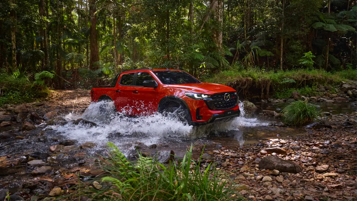 A red 2025 Mazda BT-50 driving through water