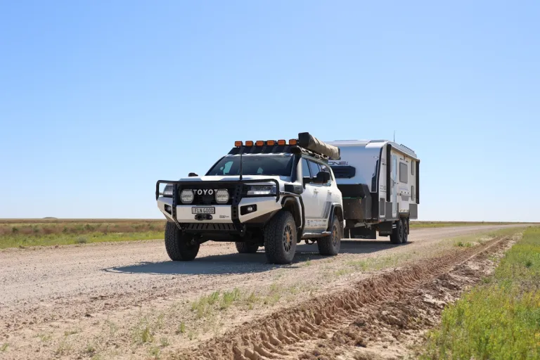 4x4 towing caravan on dirt road with blue sky