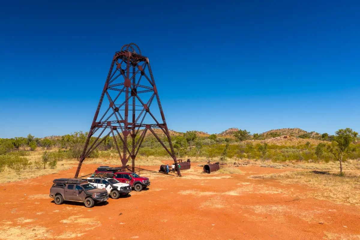 3 4X4s parked under an old structure with three people stood in the background