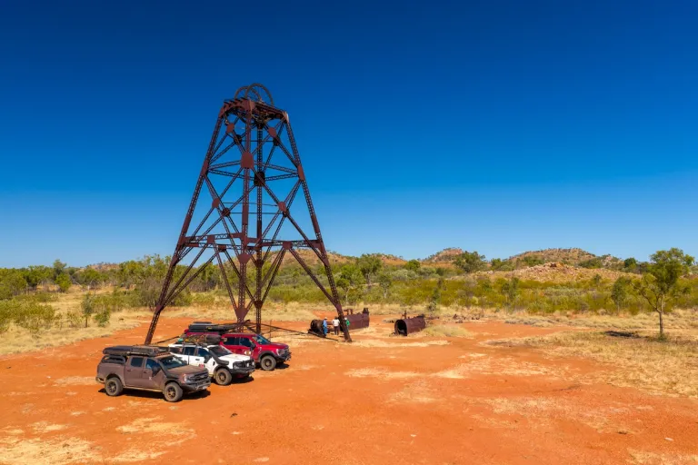3 4X4s parked under an old structure with three people stood in the background