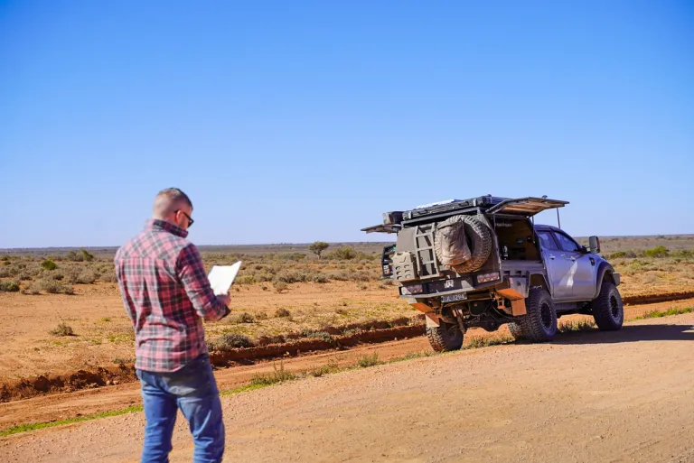 man standing with a 4wd in the outback looking at a piece of paper