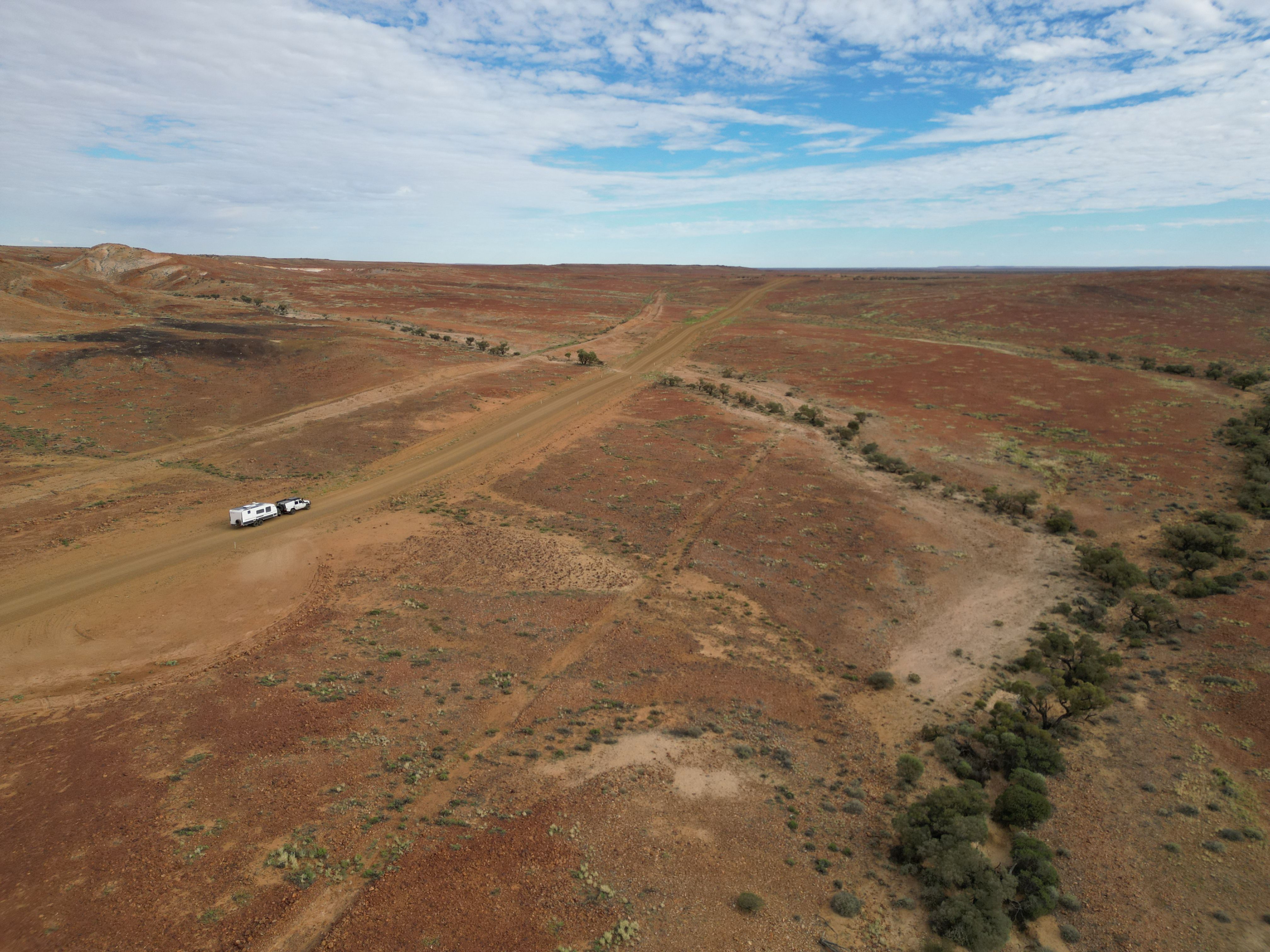 drone shot of a white Toyota LandCruiser 4X4 towing a caravan through an arid Australian landscape