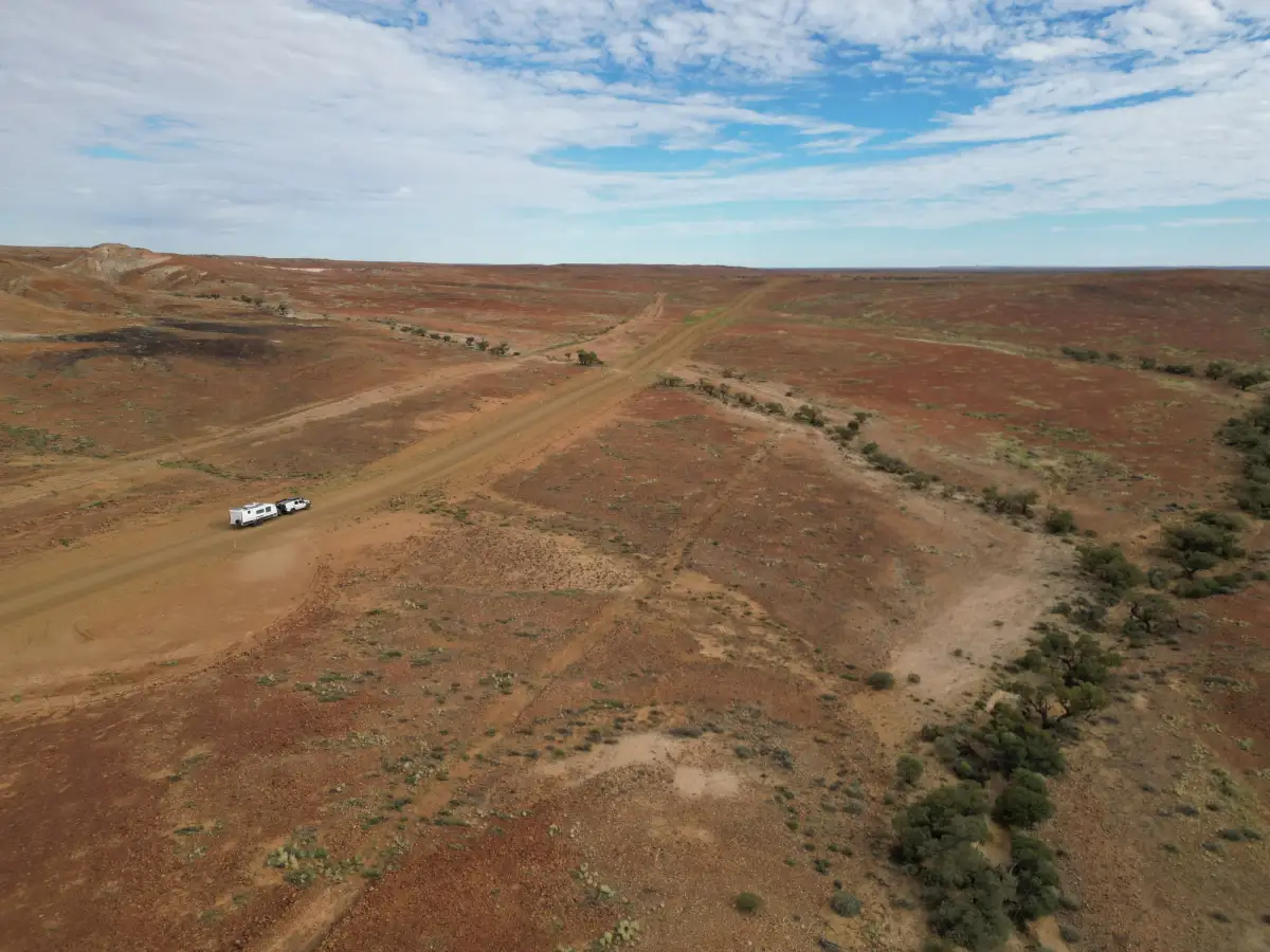 drone shot of a white Toyota LandCruiser 4X4 towing a caravan through an arid Australian landscape
