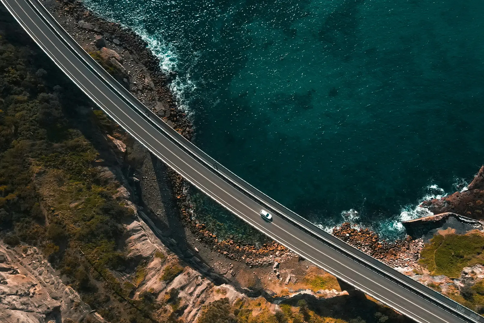 A vehicle driving over a bridge across a part of ocean