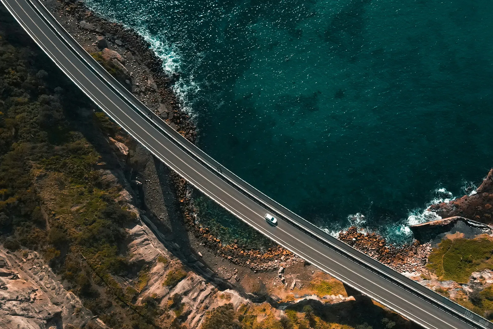 A vehicle driving over a bridge across a part of ocean